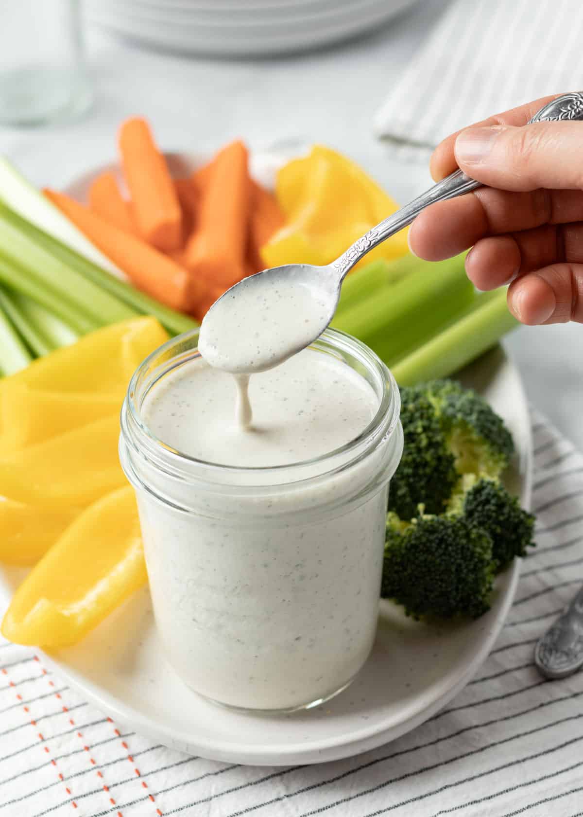 Drizzling healthy ranch dressing from a spoon to show the consistency.