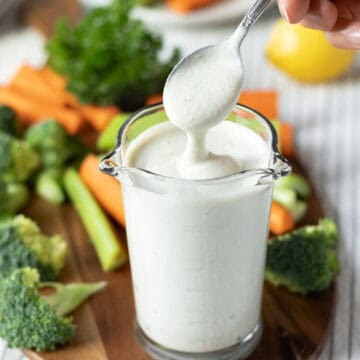 Dipping a spoon into a glass of homemade vegan ranch to show the creamy consistency.