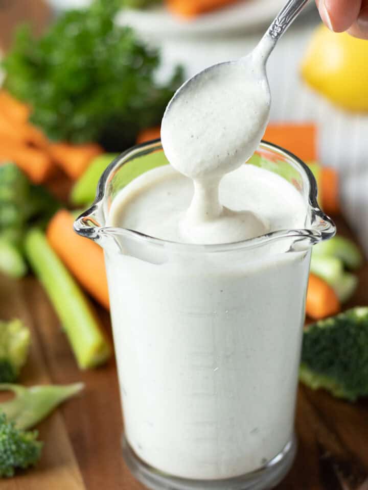 Dipping a spoon into a glass of homemade vegan ranch to show the creamy consistency.