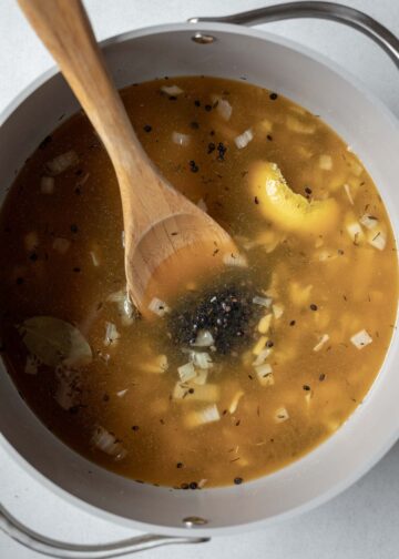 Black lentils cooking in a pot with a wooden spoon in it.