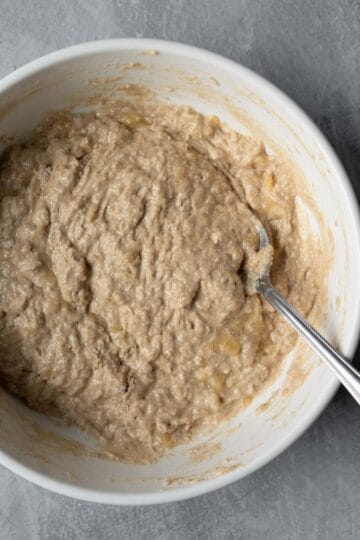 Wet and dry ingredients for banana coffee cake muffins combined in a white bowl with a fork in it.