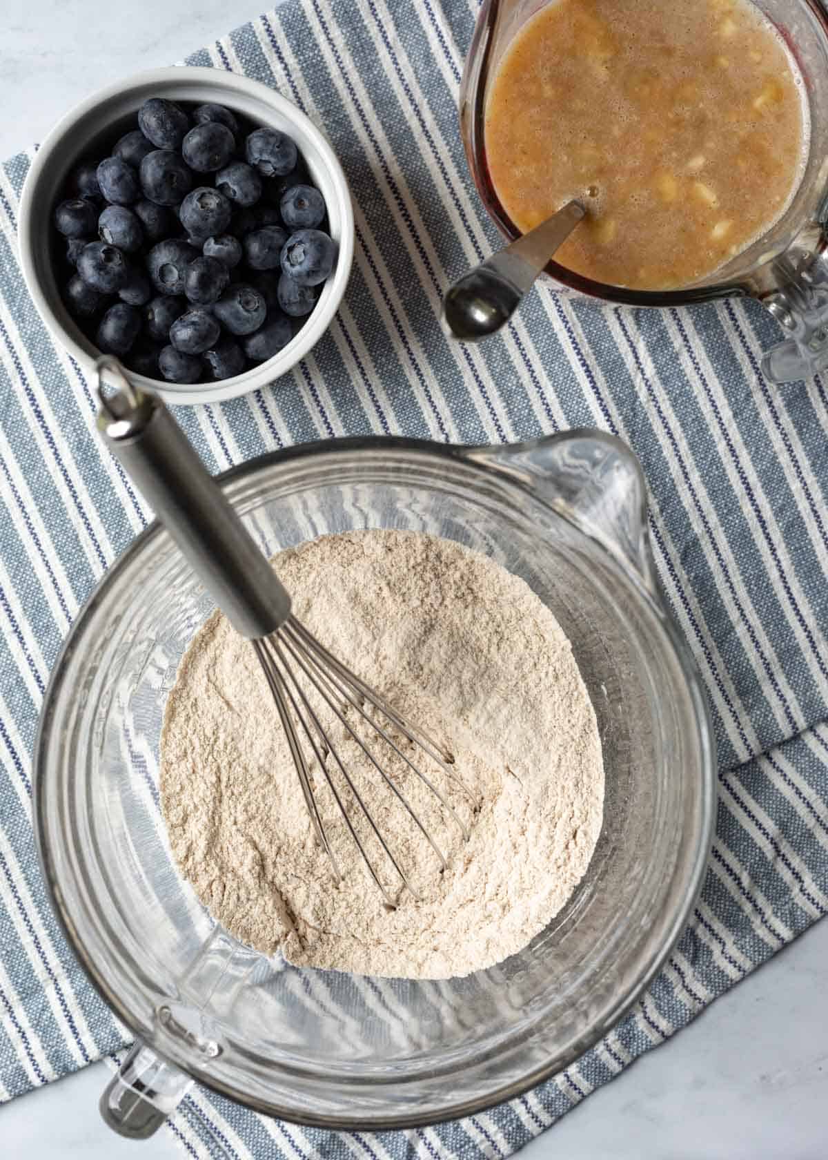 Three bowls showing wet and dry ingredients separately with fresh blueberries to the side.