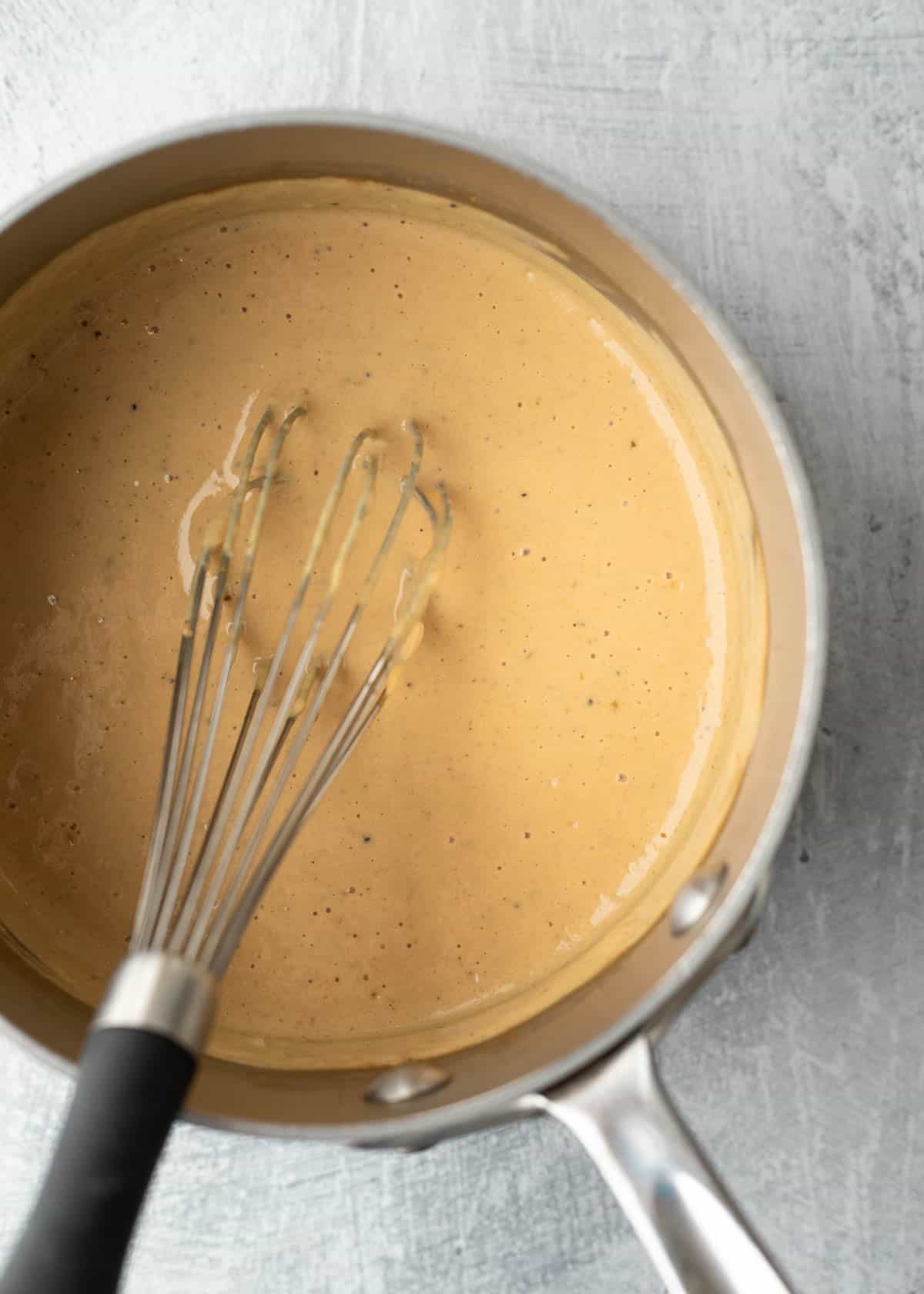 Whisking tofu queso in a saucepan.