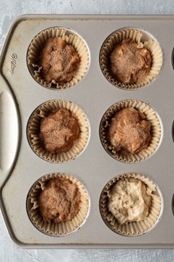 Batter added to a muffin tin with cinnamon sugar sprinkled on top of most of the cups.