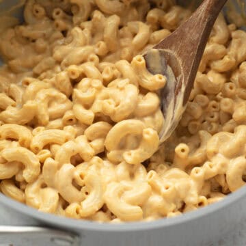 Spooning up creamy tofu macaroni from a large pot.