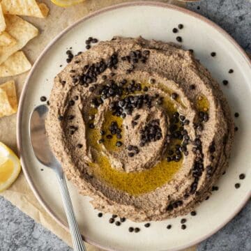 A serving plate with black lentil hummus topped with swirls of olive oil and crispy lentils.