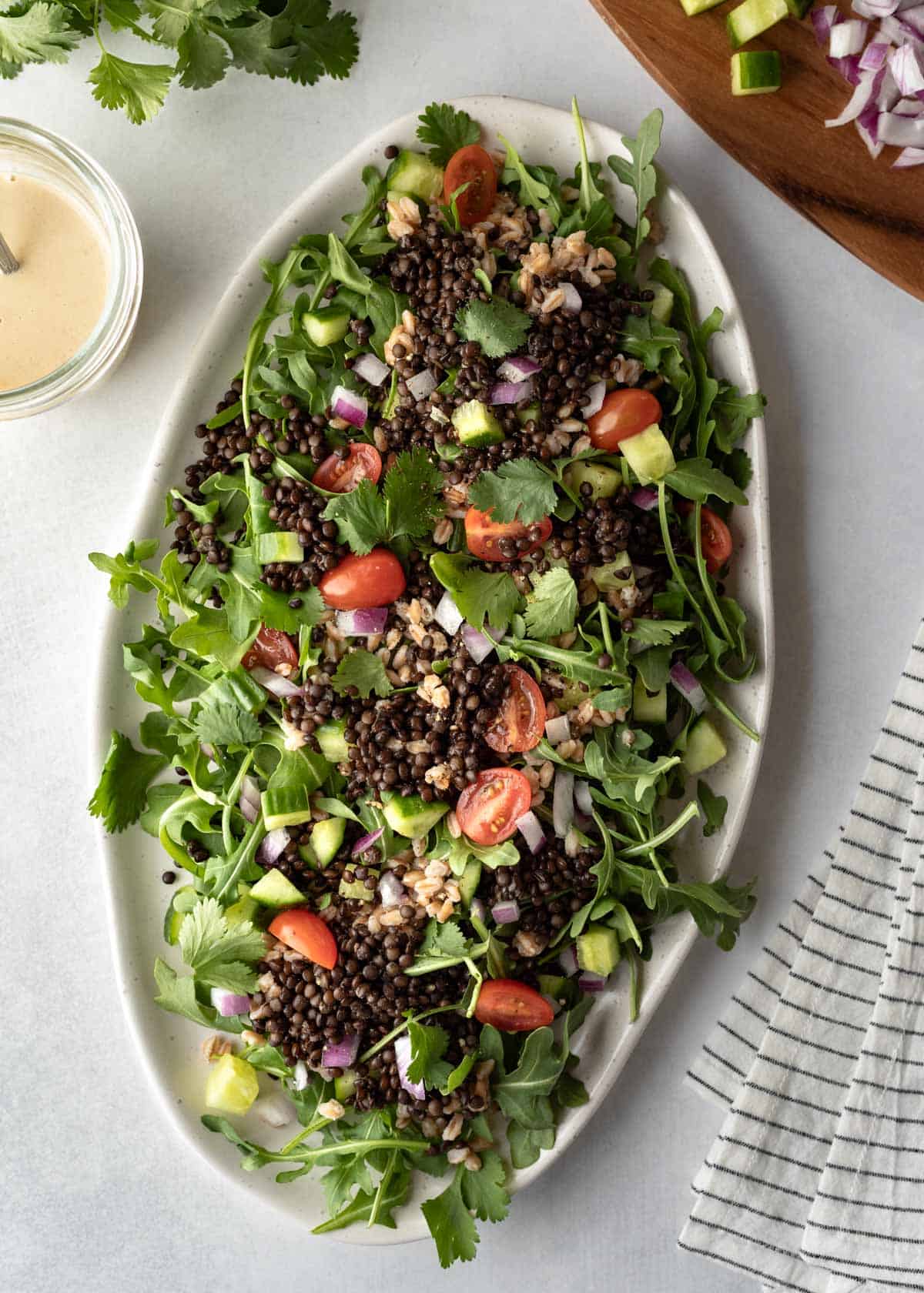 An arugula salad topped with black beluga lentils on a large serving platter.