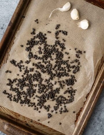 Lentils and garlic on a parchment-lined baking sheet.