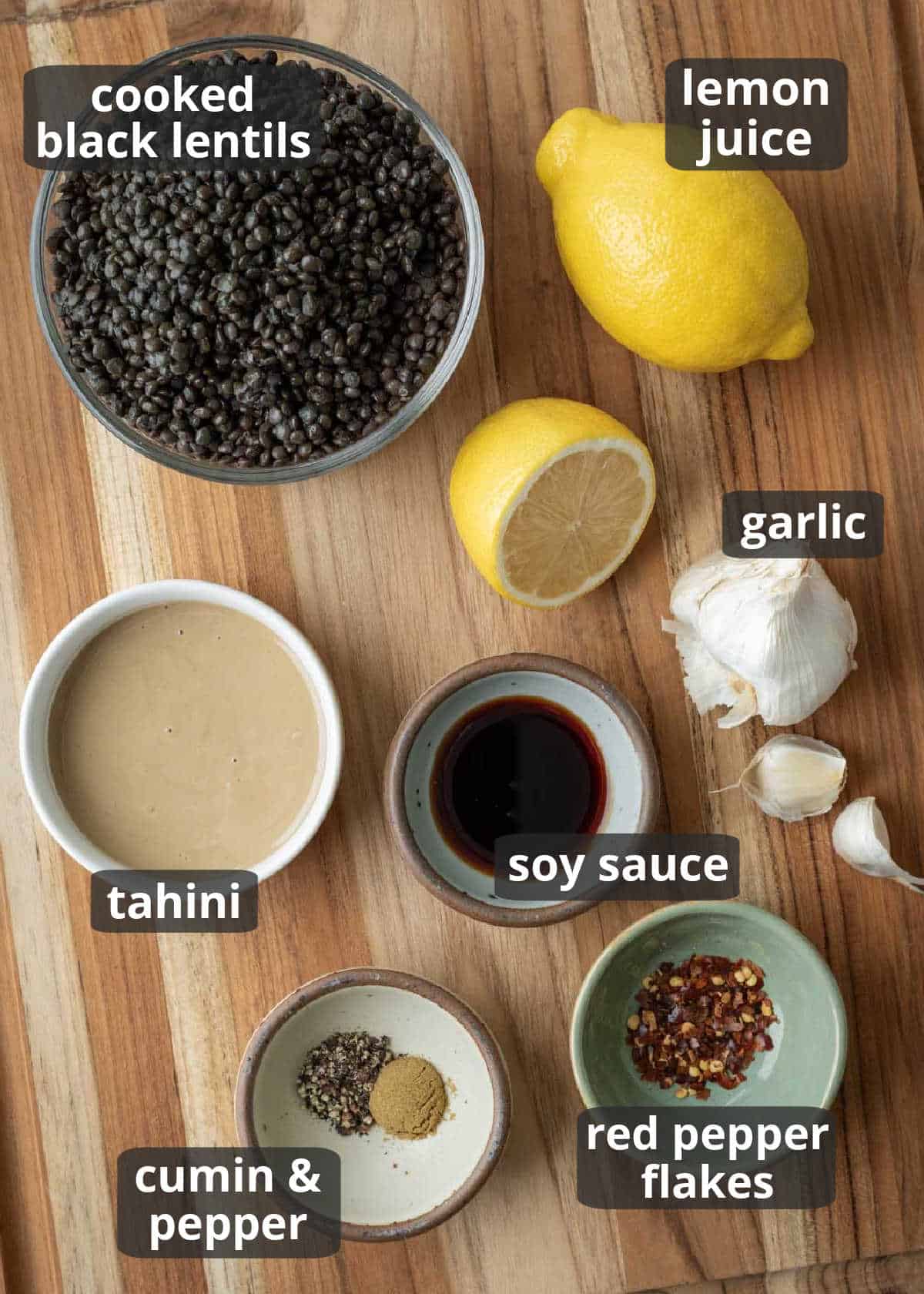 Ingredients for black lentil dip on a wooden board with text labels.