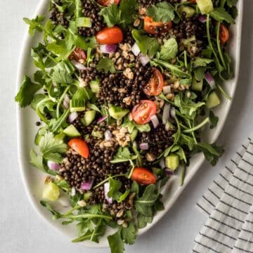 A green salad on a serving dish topped with black lentils.