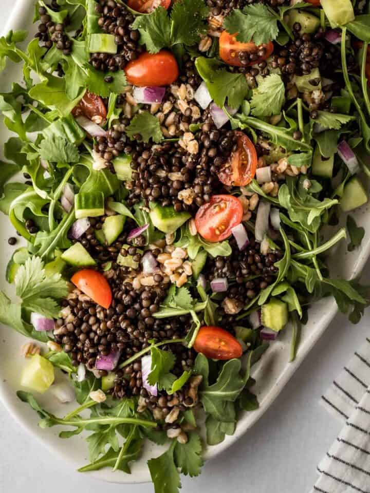 A green salad on a serving dish topped with black lentils.