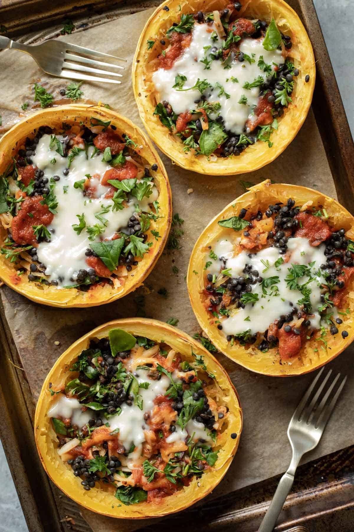 Four stuffed spaghetti squash rings arranged on a parchment-lined baking sheet.