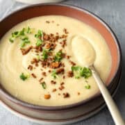 A bowl of creamy cauliflower soup topped with crumbled vegan bacon bits.