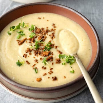 A bowl of creamy cauliflower soup topped with crumbled vegan bacon bits.