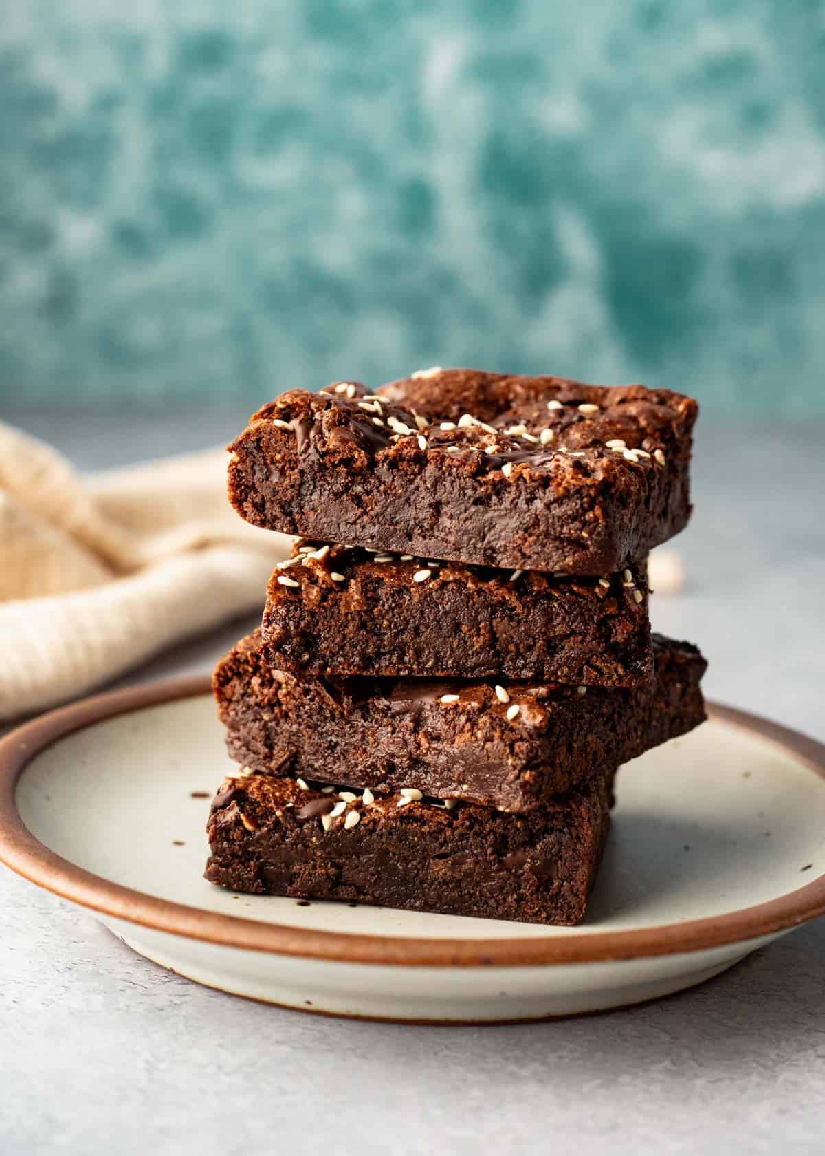 A stack of vegan buckwheat brownies on a small plate against an aqua-blue background.