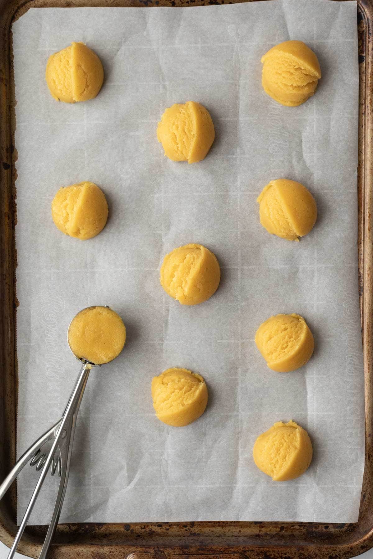 A small cookie scoop placing balls of cornmeal cookie dough on a baking sheet.