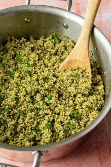 A large wood spoon folding fresh cilantro into the cooked spinach quinoa.