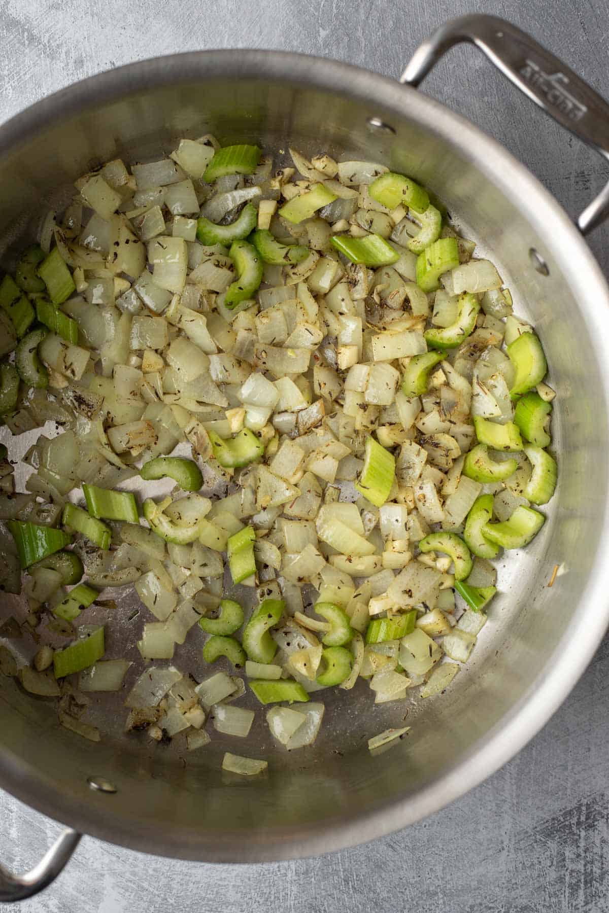 Looking inside a soup pot at sauteed onion, celery, garlic, and dried herbs.