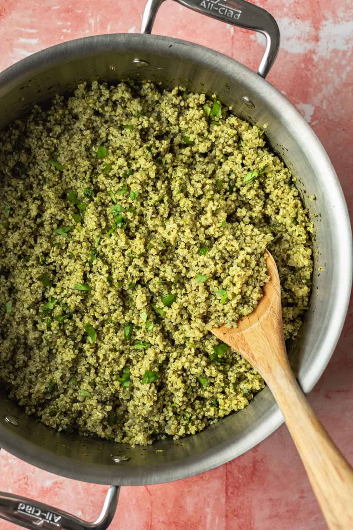 A serving spoon scooping up green quinoa from a pot.