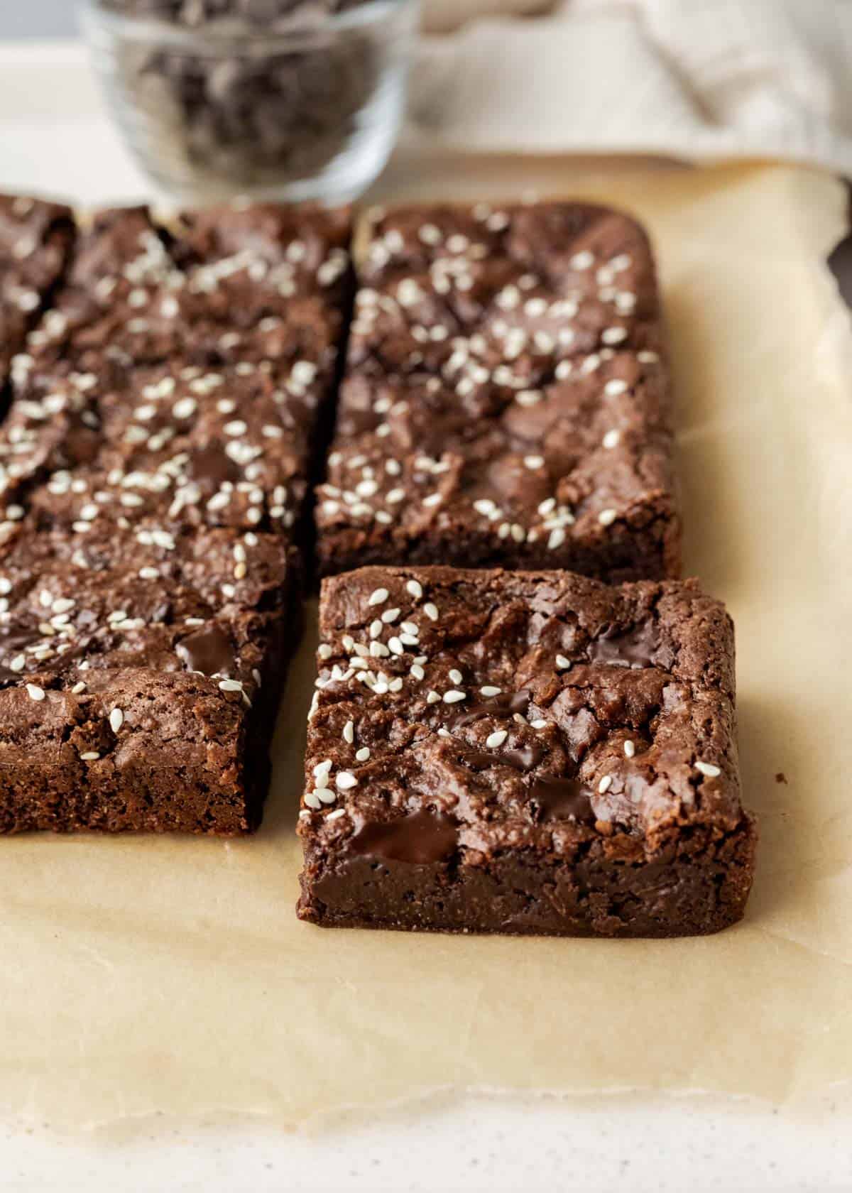 Sliced brownies on parchment paper with sesame seeds and chunks of chocolate on top.