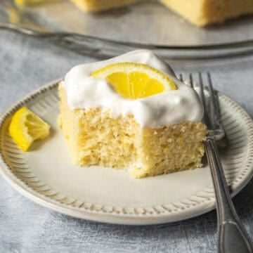 A small plate holding a slice of lemon cake topped with vegan whipped cream.