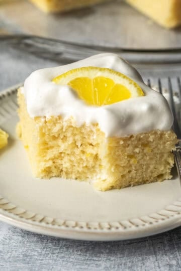 A small plate holding a slice of lemon cake topped with vegan whipped cream.