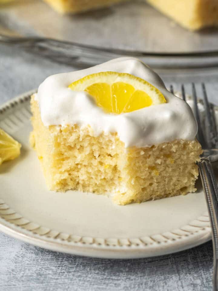 A small plate holding a slice of lemon cake topped with vegan whipped cream.