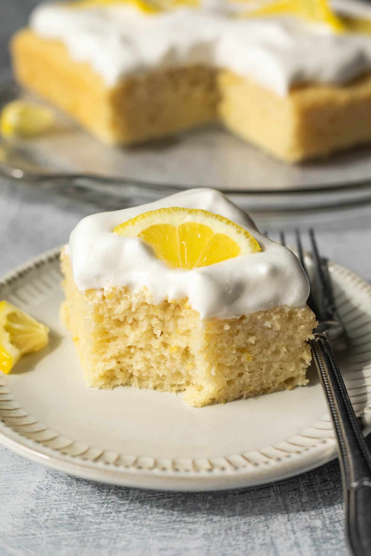 A piece of vegan lemon cake on a plate with a bite taken out showing the moist texture.