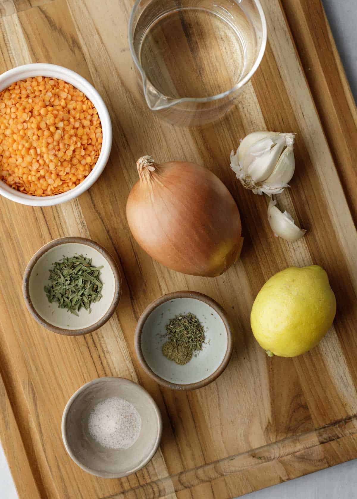 Ingredients needed for red lentil soup with herbs laid out on a wood cutting board.