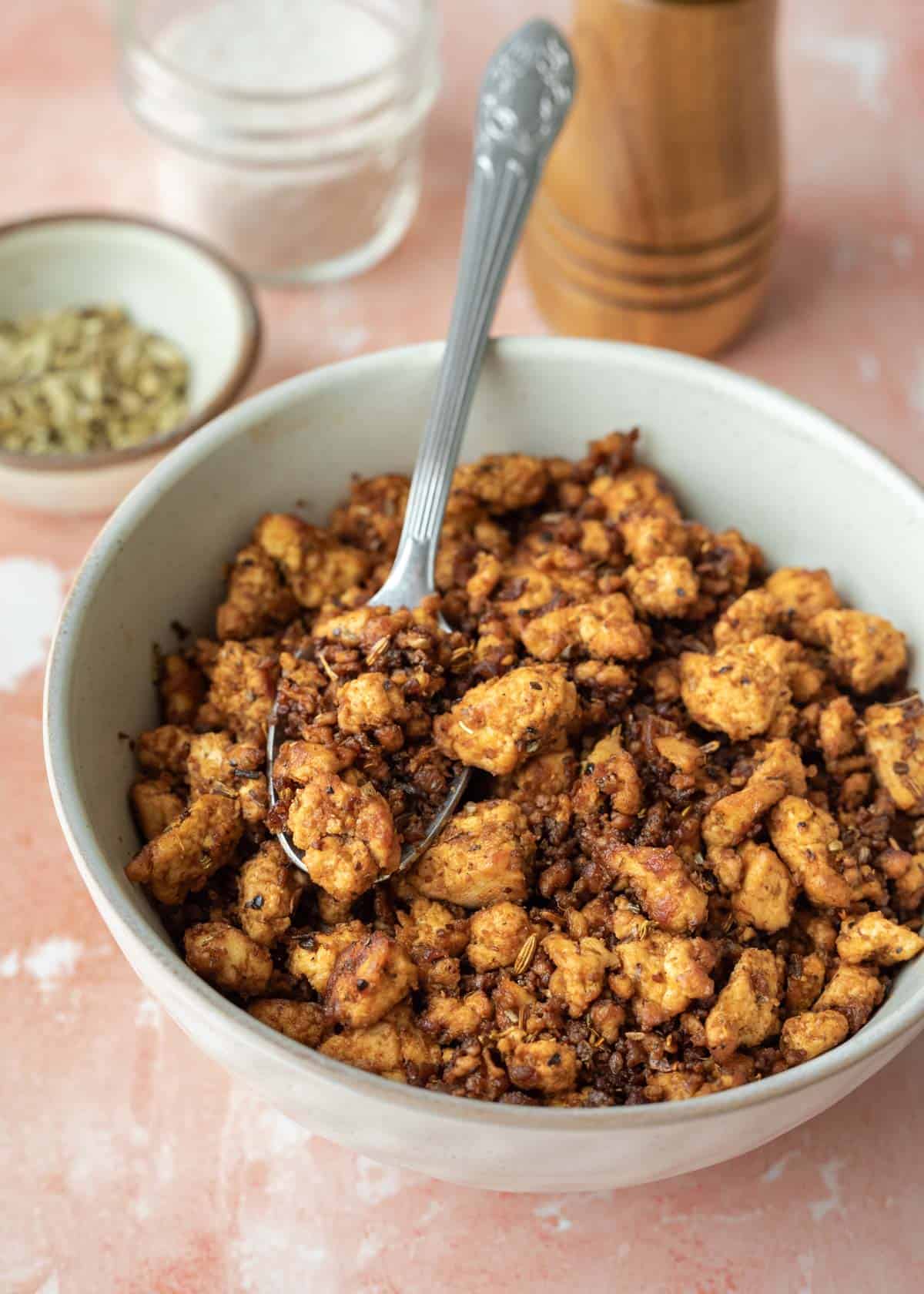 A spoon scooping up sausage tofu crumbles from a bowl.