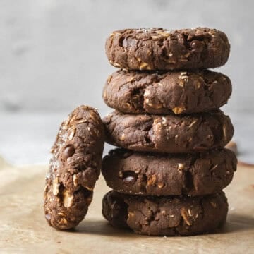 A stack of 5 chocolate protein cookies with one cookie leaning against.