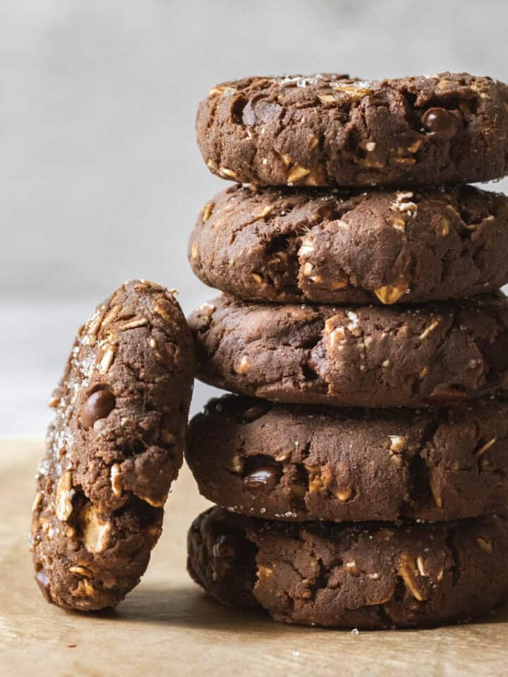 A stack of 5 chocolate protein cookies with one cookie leaning against.