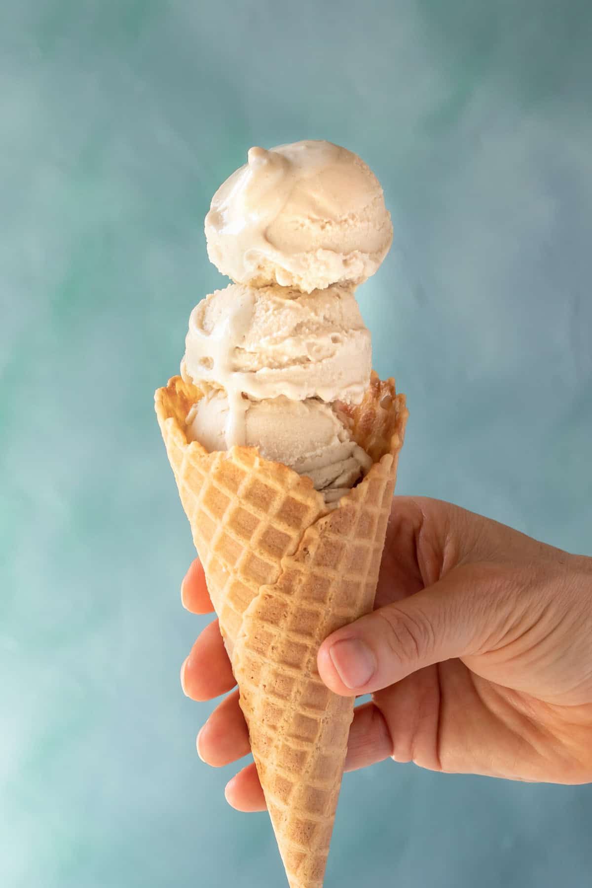 Three scoops of vanilla oat milk ice cream in a waffle cone held by the author.