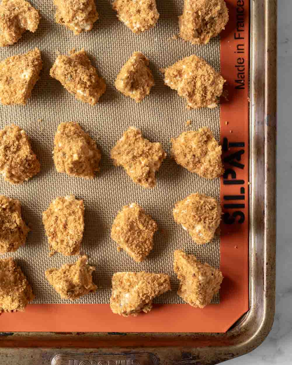 Seasoned and breaded chunks of tofu on a baking sheet ready to go into the oven.