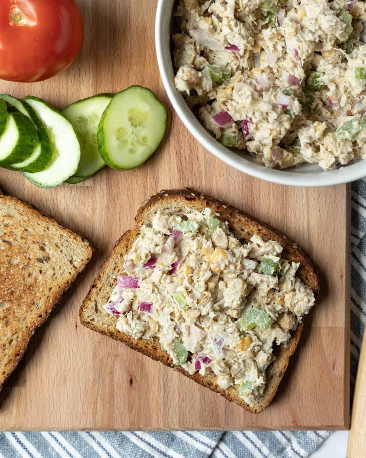 An open-face chickpea chicken salad sandwich on a cutting board.