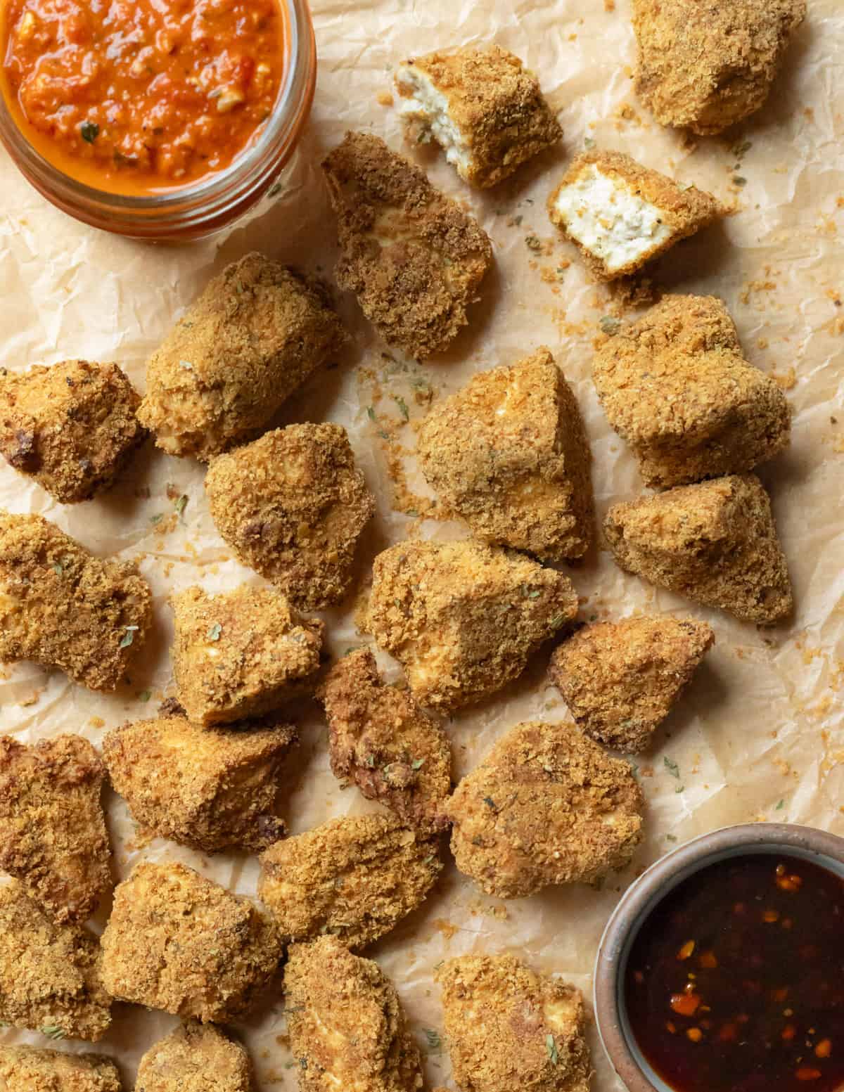 Tofu nuggets on parchment paper with sauces and one showing inside texture.