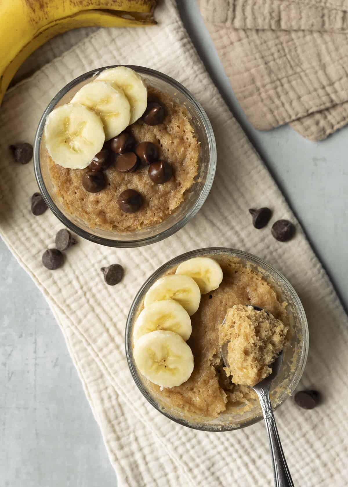 Two banana mug cakes with sliced banana and chocolate chips on top.
