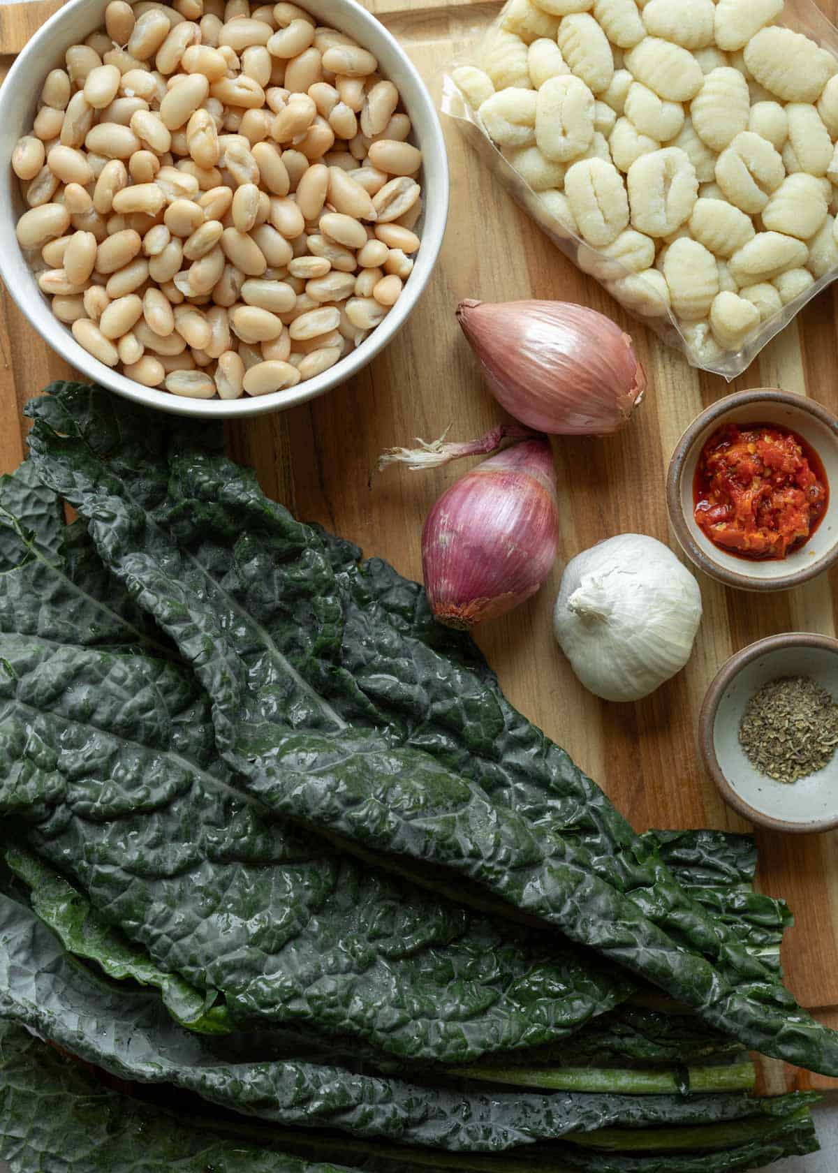 Ingredients needed for beans and greens with gnocchi and Calabrian chili laid out on a wood cutting board.