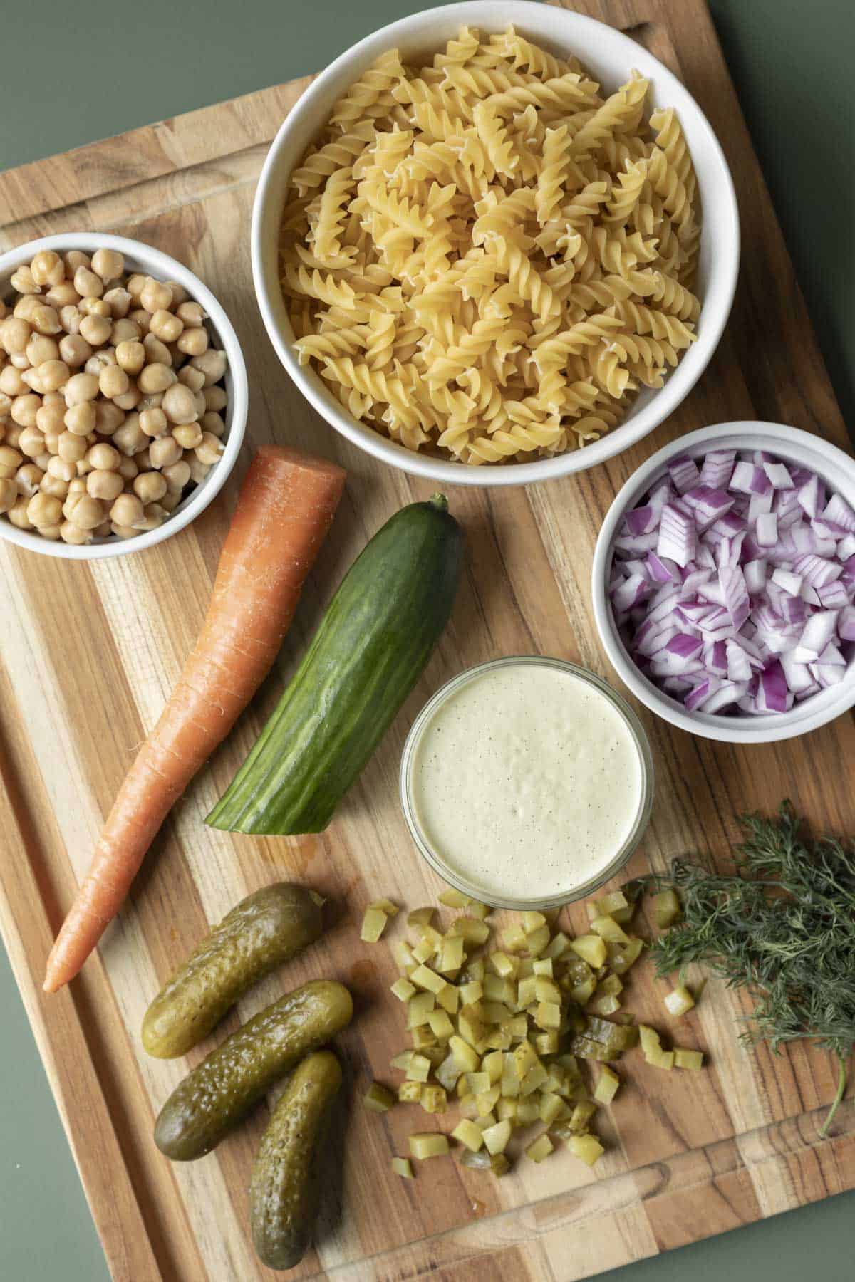 Ingredients for dill pickle pasta salad laid out on a cutting board.
