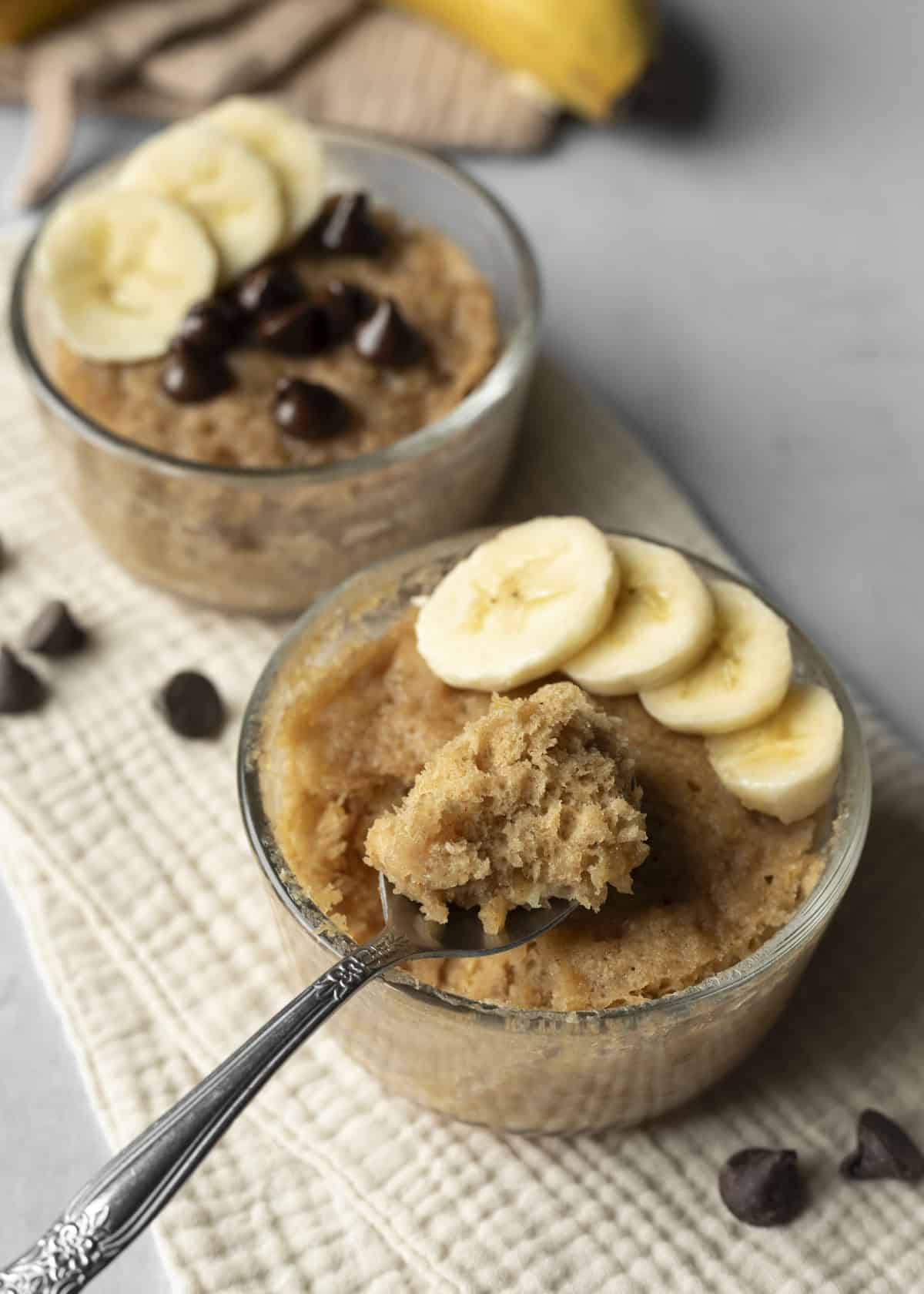 Two servings of microwave banana mug cake with a bite on a spoon to show texture.