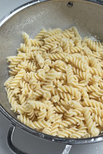 Draining rotini pasta in a colander and rinsing with cold water.