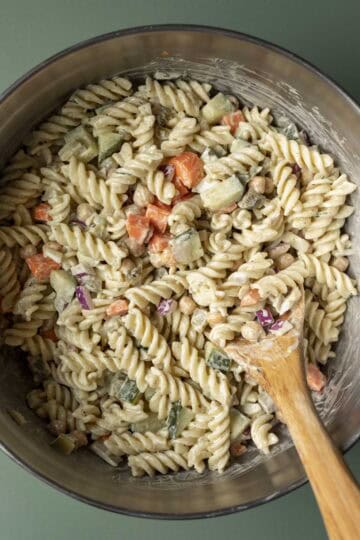 Combining the fresh veggies, pickle dressing, and cooked pasta in a large bowl.