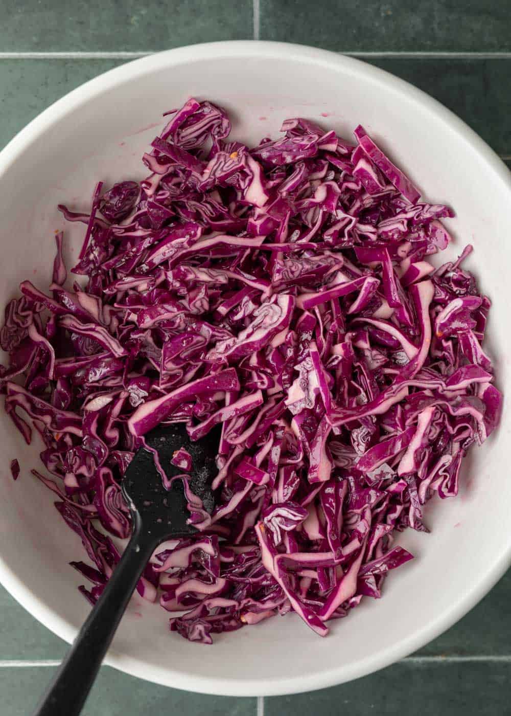Tossing shredded red cabbage with Asian dressing.