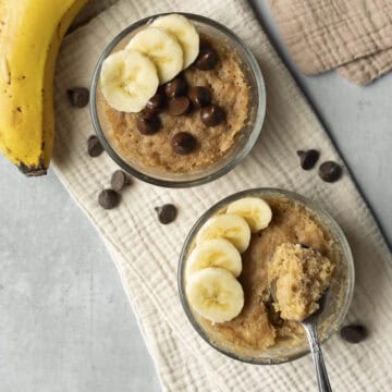 Overhead view of two microwave banana bread mug cakes topped with sliced banana.
