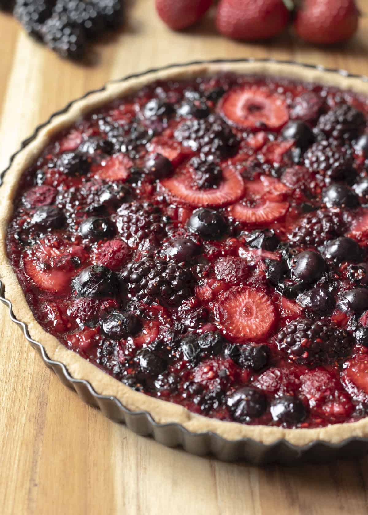 Side view of a freshly baked berry tart cooling on a wood countertop.