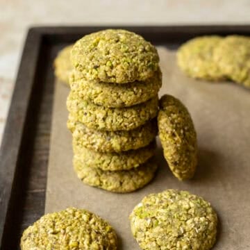 A stack of 6 pistachio cookies on parchment paper with other cookies nearby.