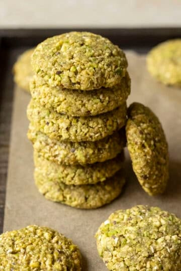 A stack of 6 pistachio cookies on parchment paper with other cookies nearby.