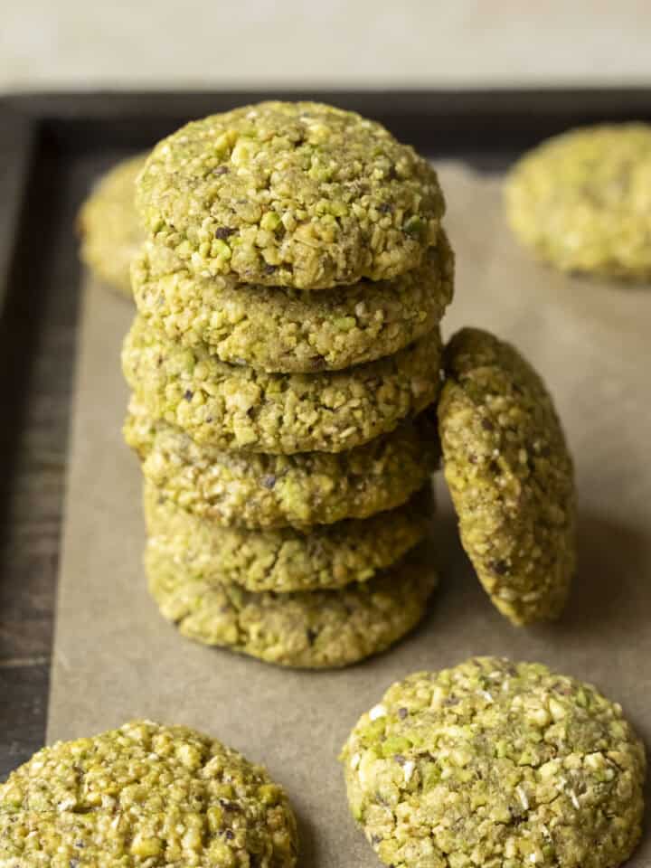 A stack of 6 pistachio cookies on parchment paper with other cookies nearby.