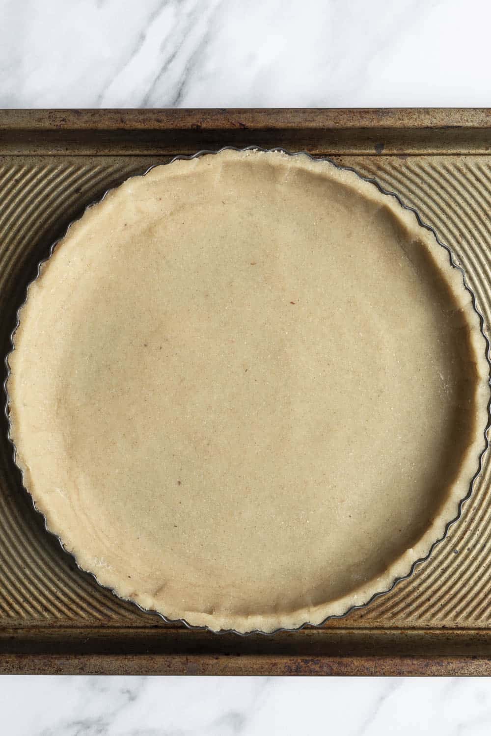 Unbaked tart shell on a baking sheet ready to be par-baked and filled.