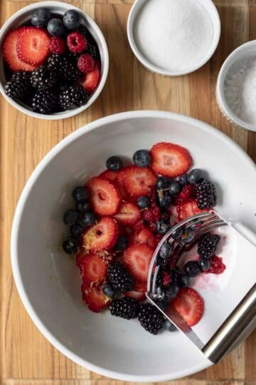 Mashing half of the berries with sugar in a large bowl.
